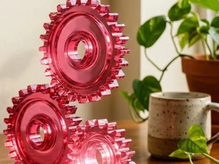 Three pink glass gears beside a plant and a mug